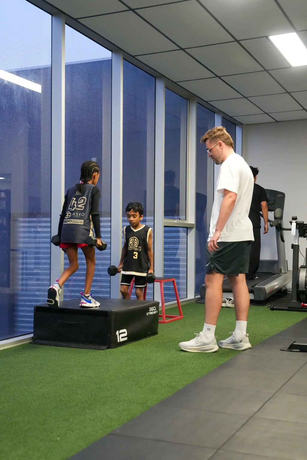 Arie coaching young athletes through a weighted step-up in the RIB gym